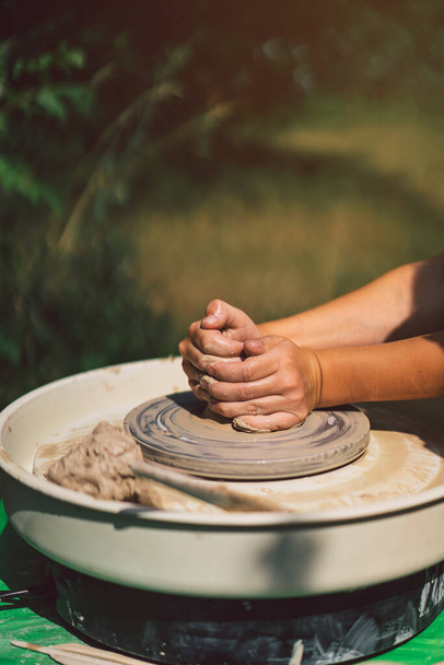 Potter making a clay object on pottery wheel in outdoors. Craftsman moulding clay with hands on pottery wheel - Photo, Image