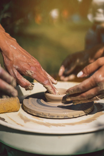 Töpfer stellt im Freien ein Tonobjekt auf einer Töpferscheibe her. Handwerker formt Ton mit den Händen auf Töpferscheibe - Foto, Bild