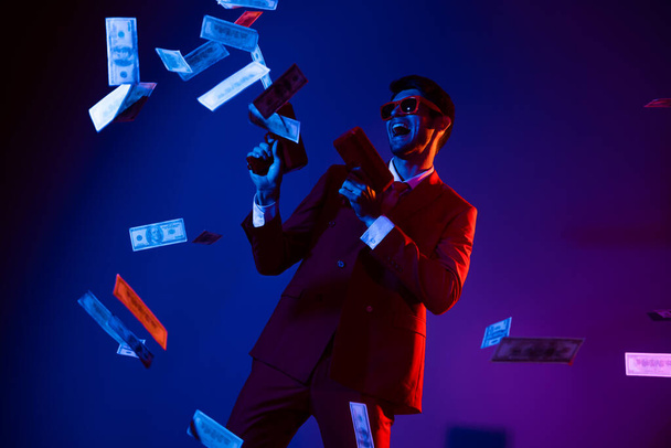 Photo of funky charming young man wear glamour costume eyewear dancing shooting money gun isolated dark blue color background - Fotó, kép