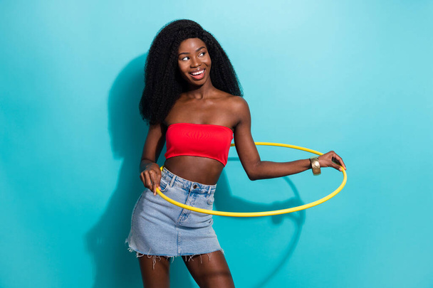 Photo of sporty pretty dark skin woman dressed top smiling holding hula hoop looking empty space isolated blue color background - 写真・画像