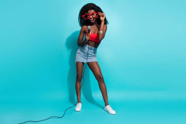 Full length photo of funky happy dark skin woman wear glasses sing mic isolated on teal color background - 写真・画像