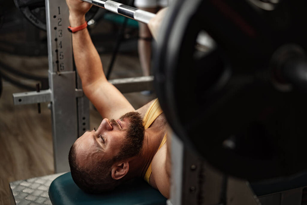 Bearded man bodybuilder doing bench press exercise in gym - Photo, Image