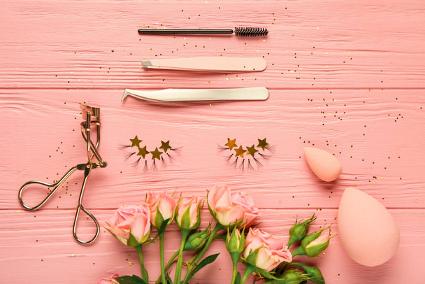 Composition with false eyelashes, tools and flowers on color wooden background - Photo, Image