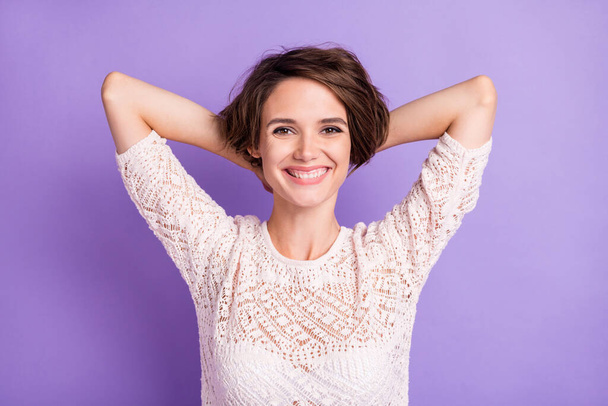 Photo of charming lady arms behind head beaming smile look camera isolated on violet color background - Foto, afbeelding