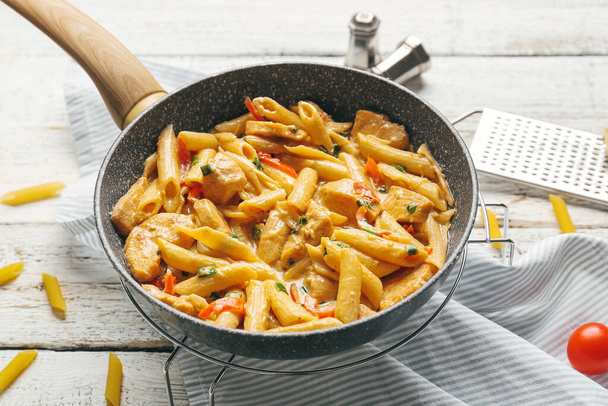Frying pan with tasty cajun chicken pasta on white wooden background - Photo, Image