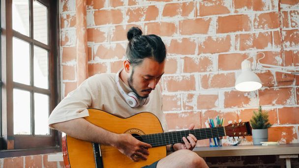 Виконавці створюють музику в домашній звуковій студії, азійський чоловік грає на гітарі і співає вдома у вітальні. Вранішнє життя чоловіка розслаблює вдома.. - Фото, зображення