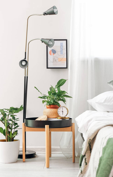 寝室のテーブルの上のスタイリッシュな目覚まし時計と観葉植物 - 写真・画像