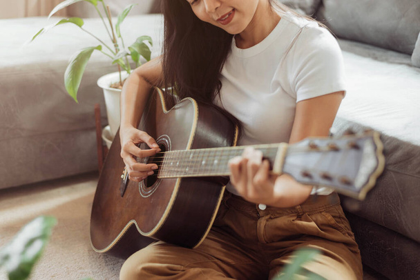 Kobieta grająca na gitarze w domu. Piękna kobieta uśmiecha się i gra na gitarze ze swoimi roślinami w salonie. - Zdjęcie, obraz