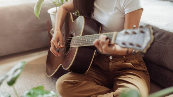 Uma mulher a tocar guitarra em casa. Mulher bonita sorrindo e tocando guitarra com suas plantas na sala de estar. - Foto, Imagem