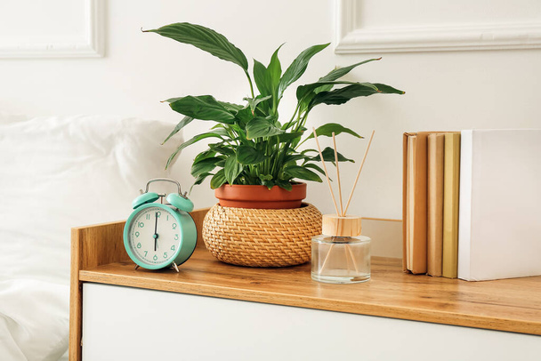 Alarm clock with houseplant and reed diffuser on shelf in bedroom - Photo, Image