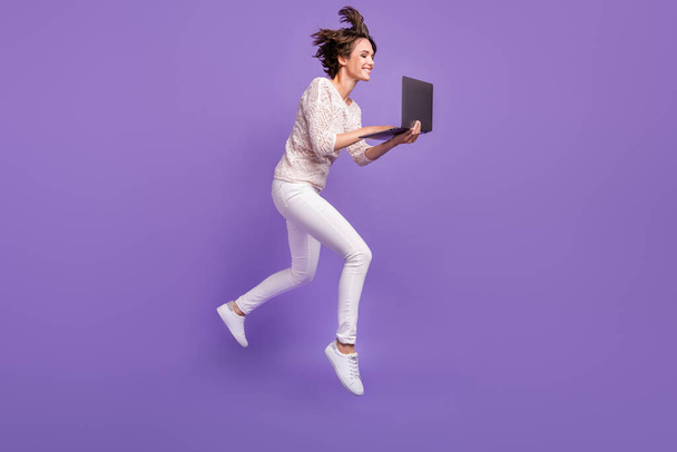 Foto in voller Länge von ziemlich lustig junge Frau tragen gestrickte Hemd springen hohe Eingabe modernes Gerät isoliert violette Farbe Hintergrund - Foto, Bild