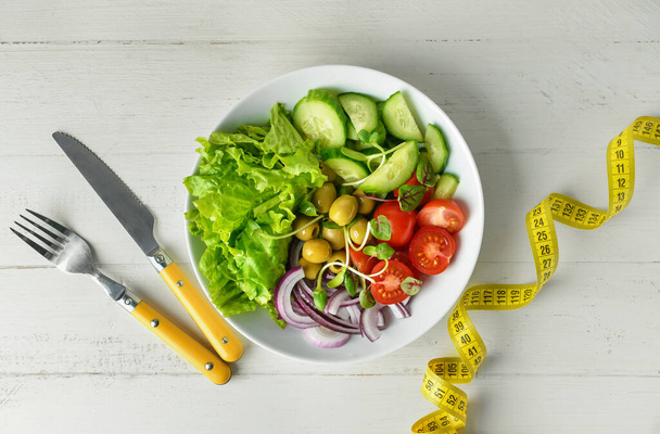 Plaat van heerlijke verse salade met groenten en meetlint op witte houten tafel - Foto, afbeelding