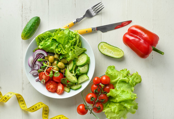 Tányér friss salátából zöldségekkel és mérőszalaggal fehér fa asztalon - Fotó, kép