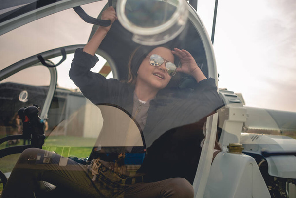 Vista a través de vidrio de cabina de helicóptero de alegre chica adolescente mirando al cielo - Foto, imagen