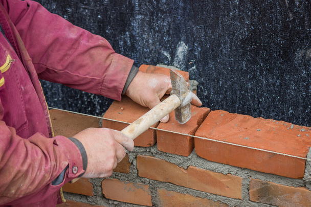 Trabalhador construtor com martelo pedreiro que estabelece tijolo de argila sólida
 - Foto, Imagem