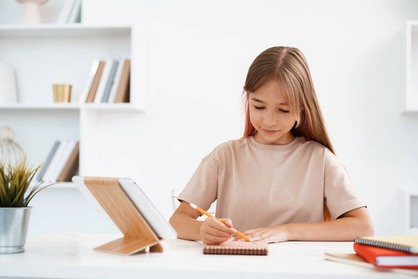 Teenage girl making notes in notepad, doing homework at table at home - Foto, Imagem