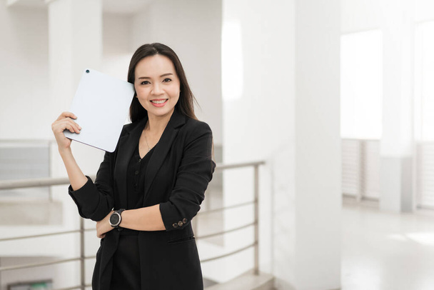 Портрет фото впевненого, веселого азіатського бізнесмена професіонала в чорному бізнес-костюмі з використанням цифрової таблетки стоячи в офісному будинку, що представляє бізнес-орієнтовану концепцію - Фото, зображення