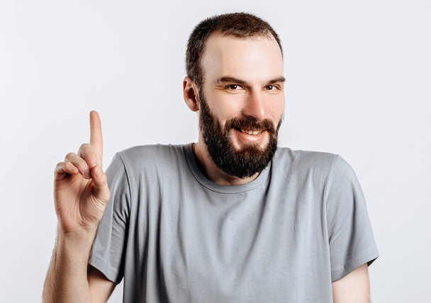 Portrait of cheerful young handsome man smiling looking at camera pointing finger upwards on white background with space for advertising mock up - Foto, immagini