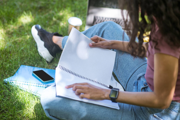 A dark-skinned woman sitting on the grass and studying - Foto, Bild