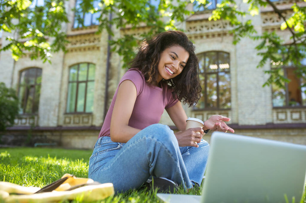 A dark-skinned woman sitting on the grass and studying - Zdjęcie, obraz