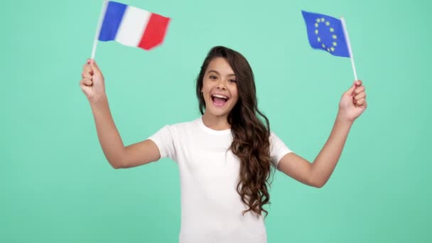 Ευτυχισμένο χαρούμενο έφηβο κορίτσι κυματίζει την Ευρωπαϊκή Ένωση και τη σημαία της Γαλλίας σε μπλε φόντο, τουριστική βίζα - Πλάνα, βίντεο