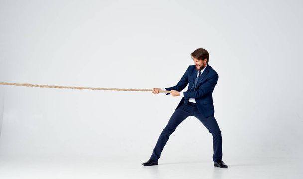 Geschäftsmann im Anzug zieht im Studio vor hellem Hintergrund das Seil. Hochwertiges Foto - Foto, Bild