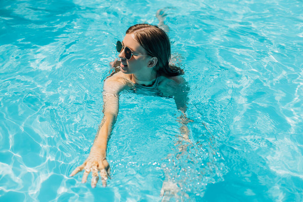 Top view, young beautiful woman in sunglasses relaxing in the water in the pool, Portrait of a happy woman in a swimsuit, floating water, relaxed woman in the pool, Summer vacation concept, travel - Φωτογραφία, εικόνα