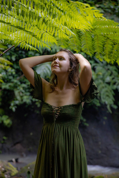 Portrait of beautiful woman under the fern leaves. Caucasian woman wearing green dress walking in tropical jungle. Nature and environment concept. Travel to Asia. Bali island, Indonesia - Фото, зображення