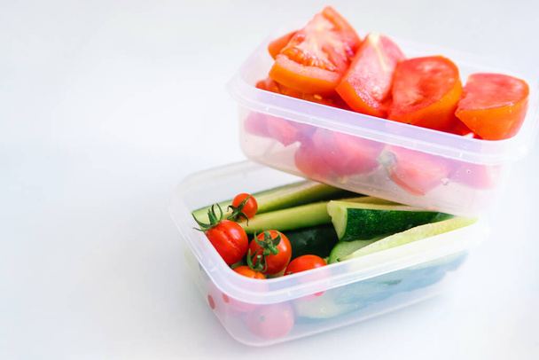 Sliced vegetables in plastic containers on a white background. Cucumbers and tomatoes are in containers. Healthy and proper nutrition. Packed lunch for work or travel. - Photo, Image