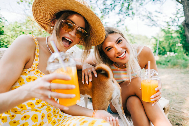 Friends having fun with dog in the backyard and drinking orange lemonade on summer sunny day. - Φωτογραφία, εικόνα