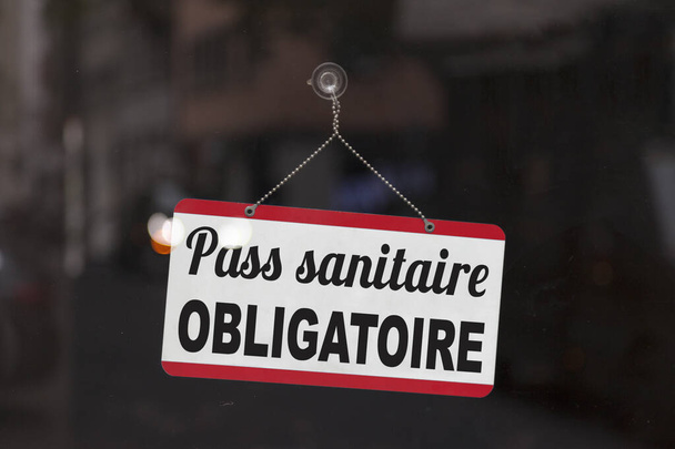 Крупный план на красно-белой вывеске в окне с надписью на французском языке "Pass sanitaire obligatoire", что означает на английском языке "Обязательный проездной"". - Фото, изображение