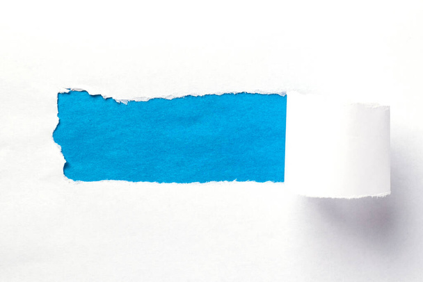 Horizontaler Hintergrund mit einem zerrissenen Loch im Papier. Hintergrund mit einem blauen Loch in weißem Papier. Zerrissenes weißes Papier auf blauem Hintergrund zusammengerollt. Durchbruchspapier. - Foto, Bild