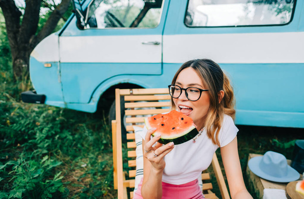 Young cheerful woman eating watermelon near van outdoors, summer traveling concept - Foto, imagen