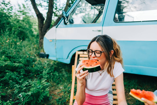 Young cheerful woman eating watermelon near van outdoors, summer traveling concept - Zdjęcie, obraz