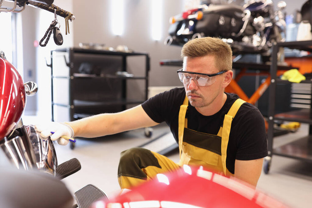 Muž opravář v brýlích vyzvednutí barvy na motocykl v autoopravně - Fotografie, Obrázek