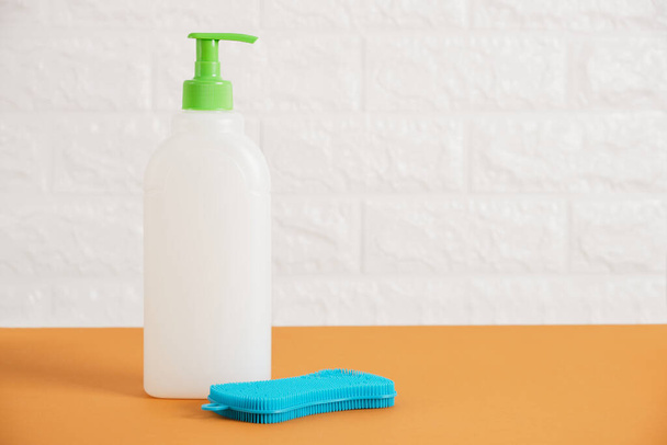 plastic blank bottle with dispenser for soap or dishwashing detergent and silicone cleaning sponge on table against white brick wall background mock up - Fotografie, Obrázek