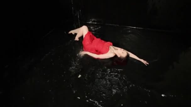 Egy piros ruhás nő örvénylik tánc közben, miközben a vízben áll.. - Felvétel, videó