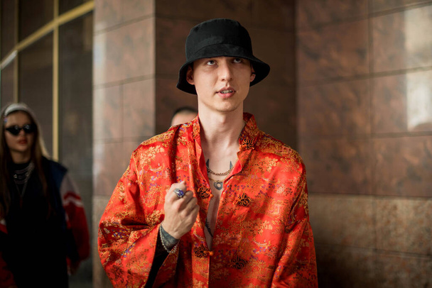 Pozytywny portret mężczyzny z ubraniami w stylu ulicy czerwone kimono z łańcuchami wokół szyi. Koncepcja młodości i stylu życia. Luksusowy raper. - Zdjęcie, obraz