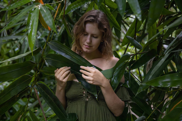 Cara de mujer rodeada de hojas de bambú. Ojos cerrados. Retrato de una hermosa mujer en la selva tropical. Plantas verdes exuberantes en la selva. Concepto de naturaleza. Isla de Bali, Indonesia - Foto, Imagen