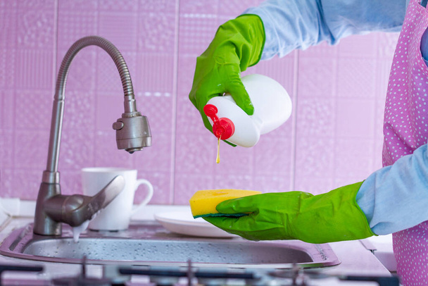 Cleaning woman in rubber gloves and apron using sponge and detergent for washing dishes at kitchen at home - Photo, Image