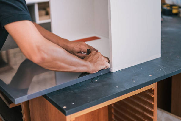 Hände eines Mannes, der ein Scharnier auf einer Oberfläche für eine Küche befestigt. - Foto, Bild