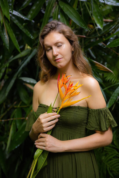 Portrét krásné ženy s květinami Heliconia v džungli. Zavřené oči. Běloška v tropickém deštném pralese v zelených šatech. Koncept přírody a životního prostředí. Cestování do Asie. Bali, Indonésie - Fotografie, Obrázek