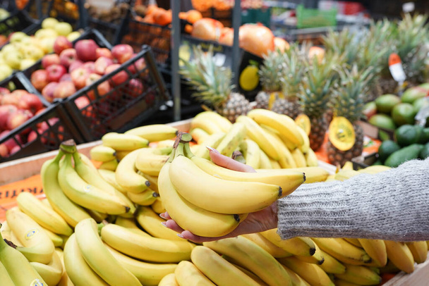 woman's hand choosing bananas from food counter in supermarket. - Photo, image