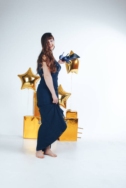 Woman dancing wearing night party dress on white background with golden inflatable star and gift boxes. Party corporate event times in epidemic, christmas and birthday concept - 写真・画像