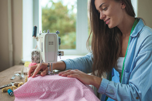 Happy smiling seamstress with electric sewing machine and different sewing accessories for sewing clothes at workplace  - Foto, immagini