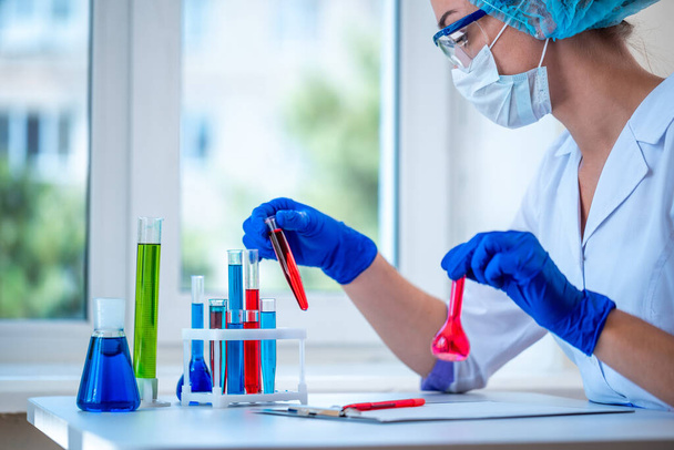La química femenina tiene tubos de ensayo en sus manos para llevar a cabo investigaciones de laboratorio clínico. Medicina, farmacia y cosmetología. Vidrio científico para ensayo  - Foto, imagen