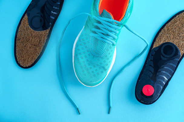 Orthopedic insoles and sneakers on a blue background. Prevention and treatment of flat feet. Foot care and wearing comfortable sports shoes - Foto, immagini