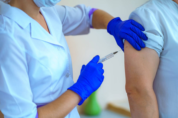Nurse in gloves vaccinated patient in hospital against flu and measles during an epidemic. Flu shot, protection and prevention of viral infectious diseases - Φωτογραφία, εικόνα