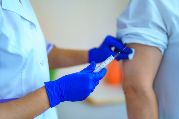 Nurse in gloves making a vaccination in the shoulder patient in hospital room. Flu shot, protection and prevention of viral infectious diseases - Foto, afbeelding