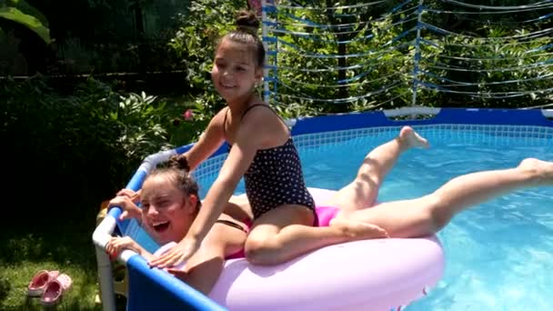 Happy children splash down from swimming ring in outdoor swimming pool, fun - Кадры, видео